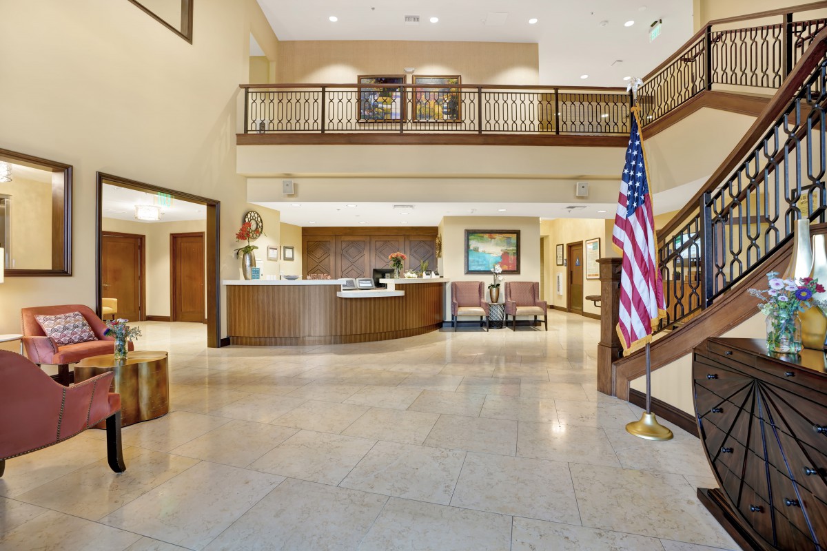 A spacious hotel lobby with a reception desk and an American flag.