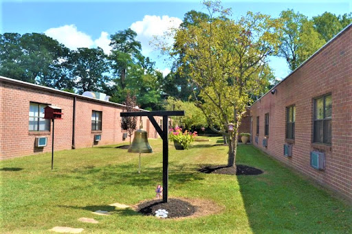 A sunny courtyard featuring brick buildings, a tree, and playground equipment.
