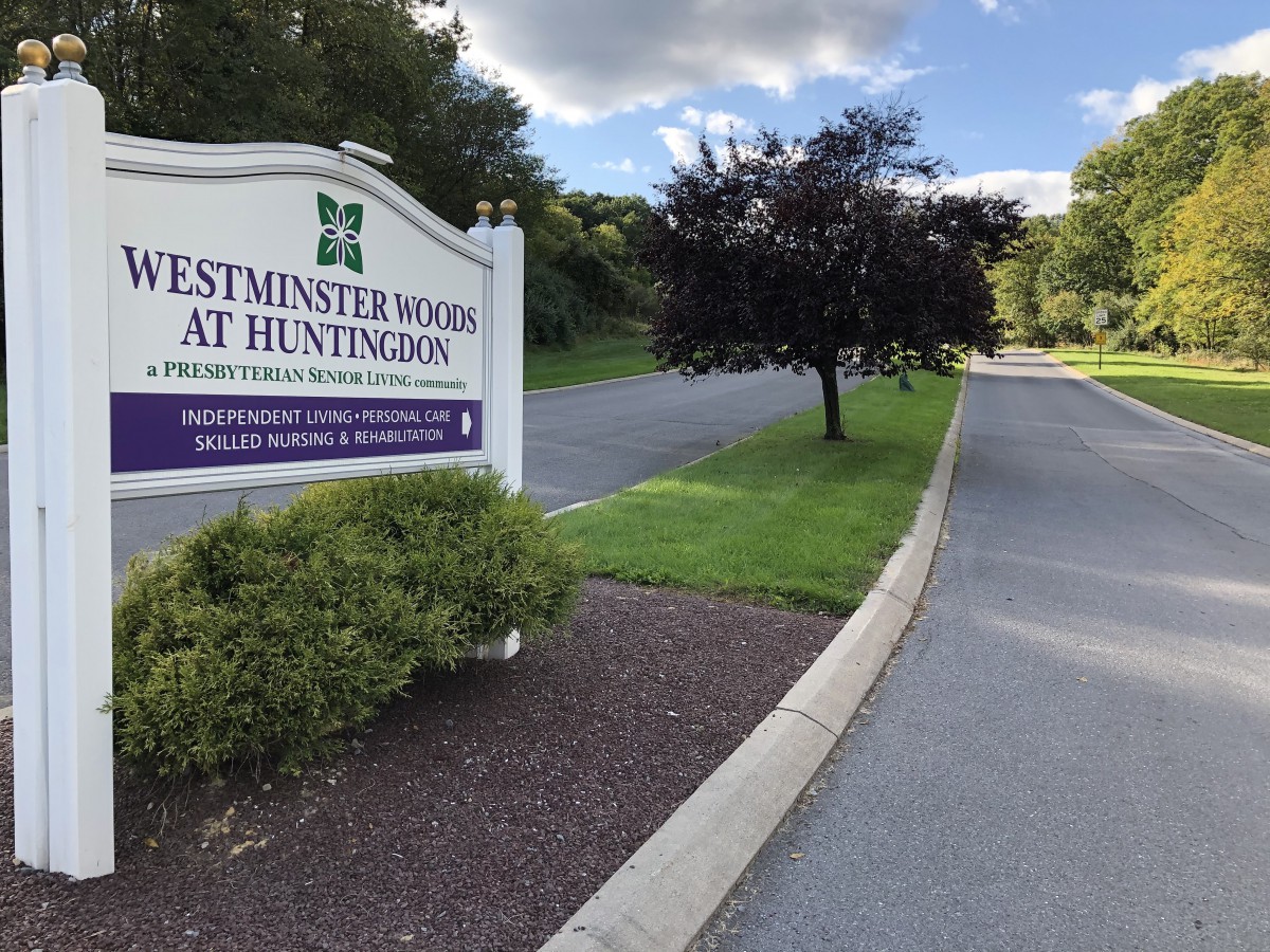 Entrance sign for Westminster Woods at Huntingdon, surrounded by trees and a road.