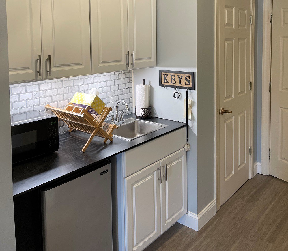 A modern kitchen with white cabinets, a black countertop, and a dish rack next to the sink.
