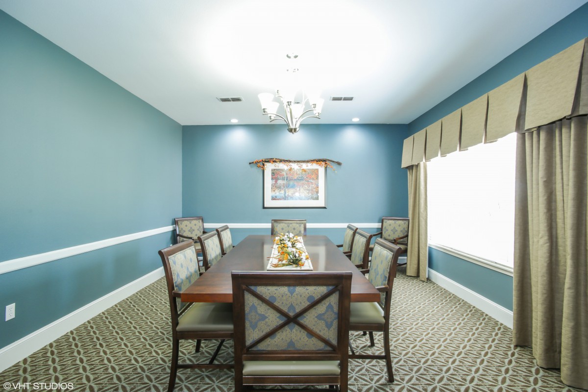 A well-lit dining room with a large table and six chairs, decorated with a chandelier and wall art.