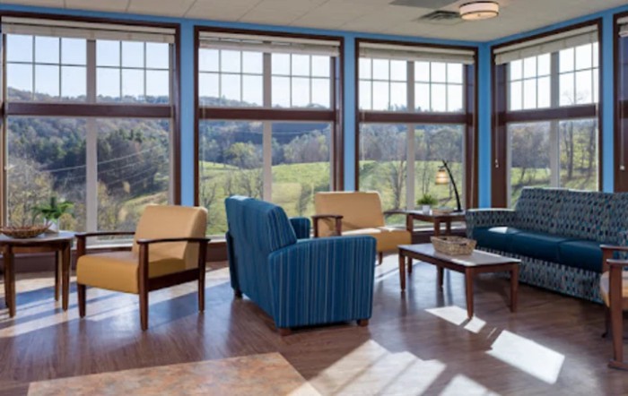 A spacious living room with large windows offering a scenic view, featuring comfortable seating and natural lighting.