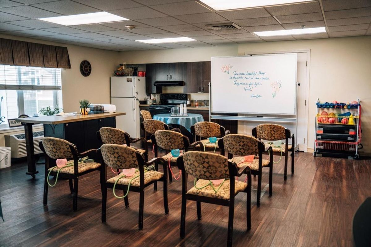 A classroom setup with chairs facing a whiteboard in a room featuring a small kitchen area.