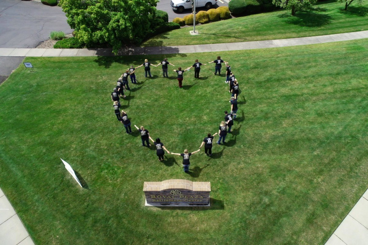 A group of people standing in a heart formation on a grassy field.