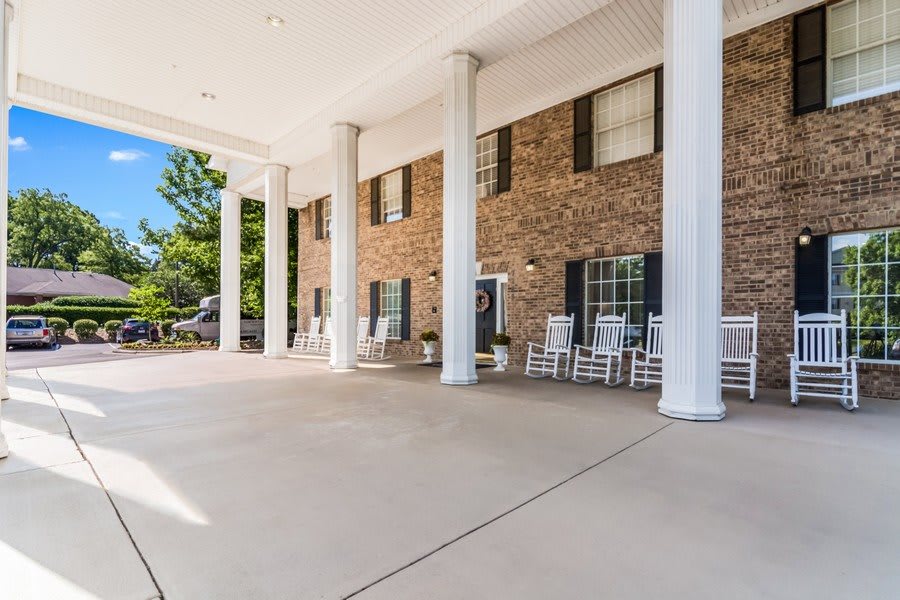 The entrance of a building with large columns and rocking chairs.