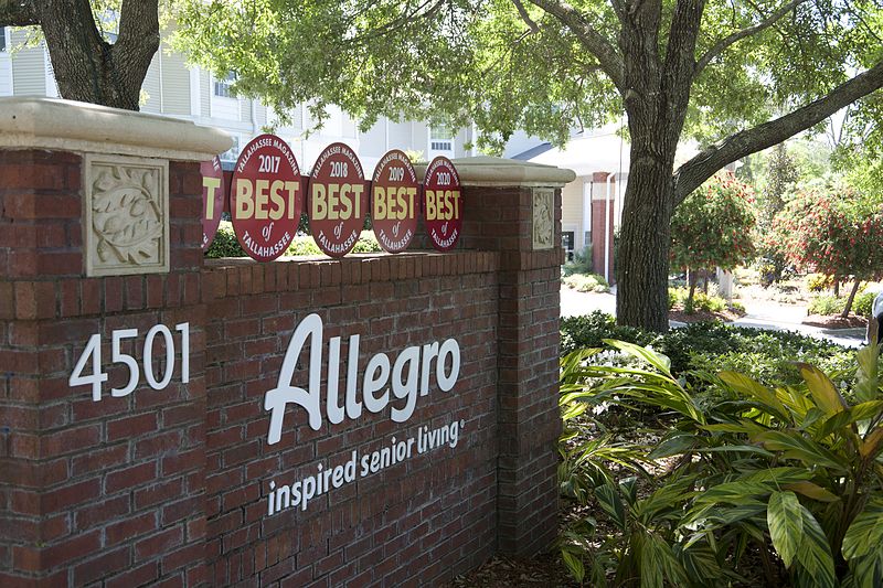 A brick sign for Allegro inspired senior living, surrounded by trees and landscaping, showcasing awards.