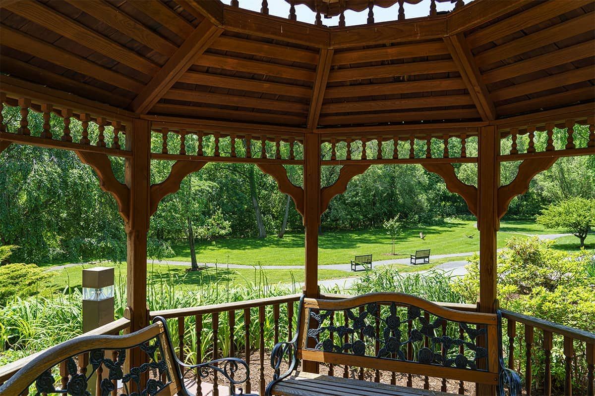 A wooden gazebo overlooking a scenic park with lush greenery.