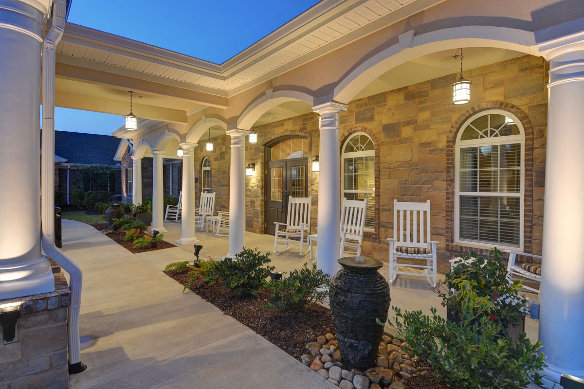 A welcoming porch with rocking chairs and elegant columns, beautifully lit in the evening.