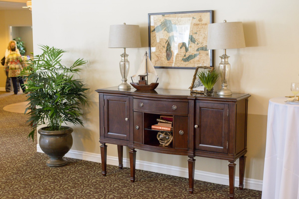 A stylish console table with two lamps, decorative items, and artwork above it, accompanied by a potted plant.