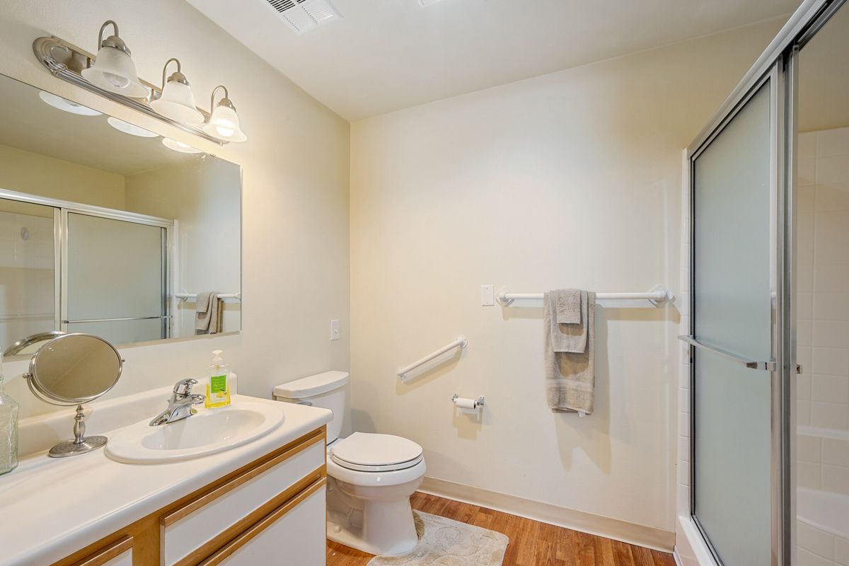 A clean and well-lit bathroom featuring a toilet, sink with mirror, and a shower.