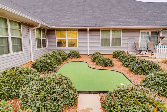 A residential courtyard with a mini golf putting green surrounded by shrubs.