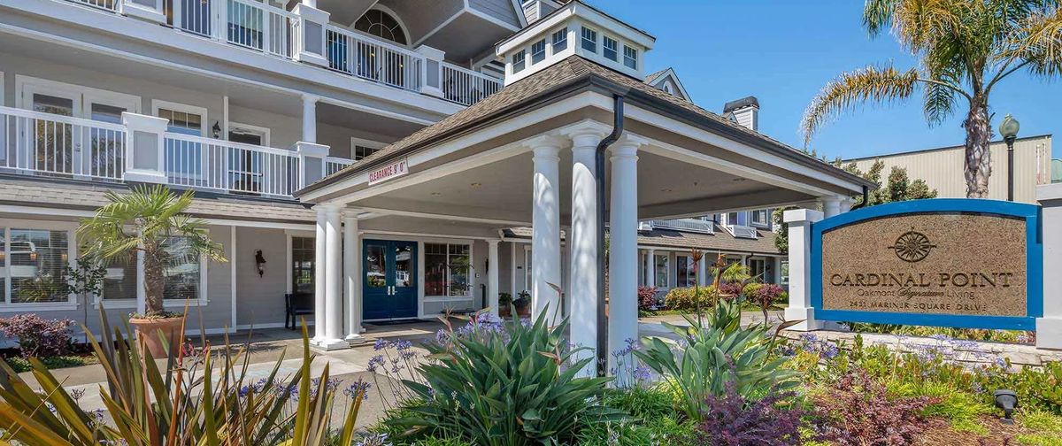 A well-maintained residential building entrance with columns and surrounding garden.