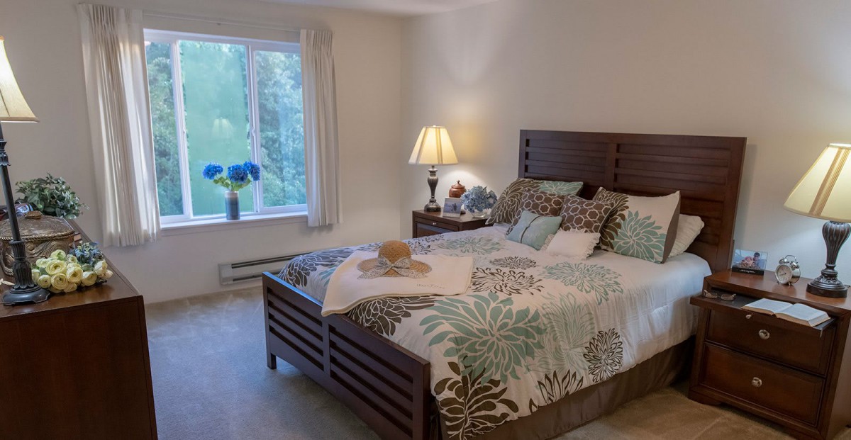 A cozy bedroom with a large bed, elegant bedding, and a side table lamp near a window.