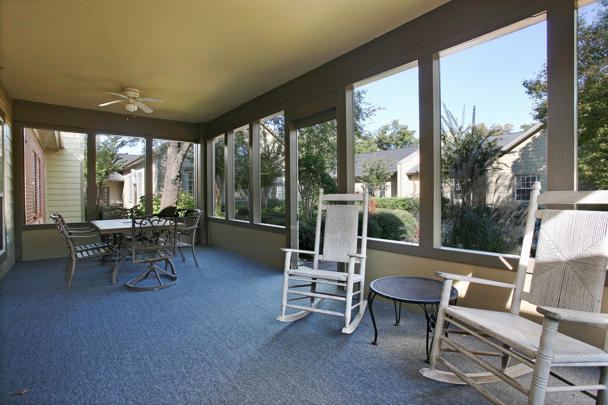 A bright sunroom with large windows, featuring rocking chairs and a dining table.
