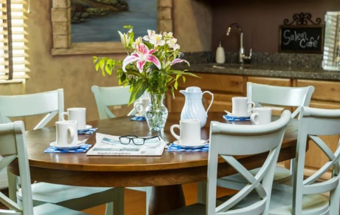 A cozy kitchen scene with a wooden dining table set for four, featuring a vase of fresh flowers and a newspaper.
