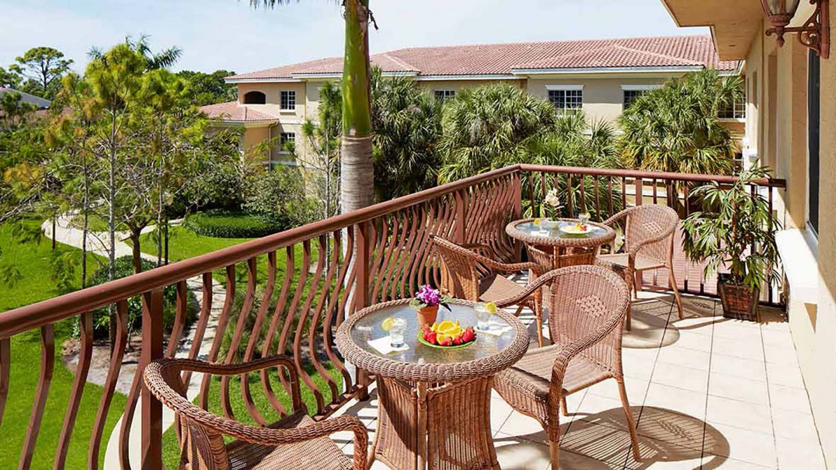 A cozy balcony with wicker tables and chairs overlooks a lush tropical garden.