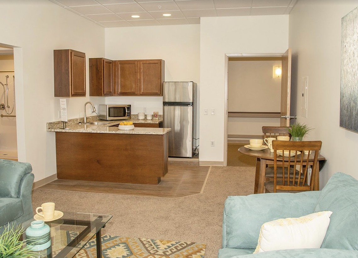 A modern open-plan kitchen and living area with wooden cabinets and stainless steel appliances.