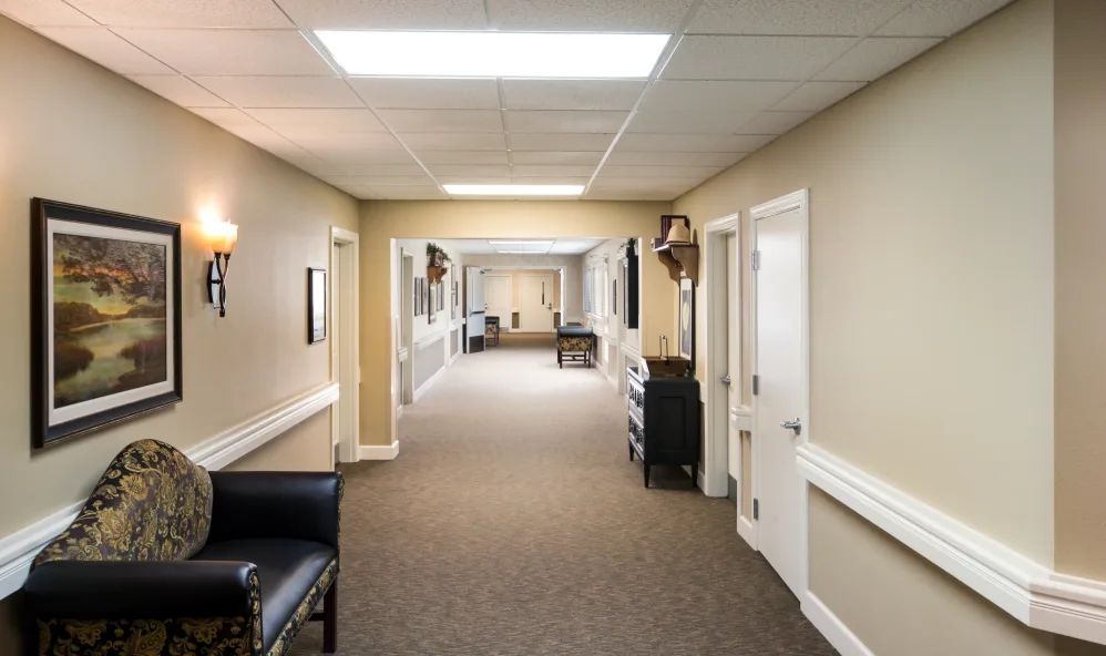 A well-lit hallway with carpeted flooring, featuring doors on each side and some decorative furniture.