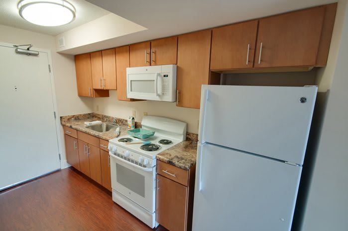 A compact kitchen with wooden cabinets, featuring a stove, microwave, and refrigerator.