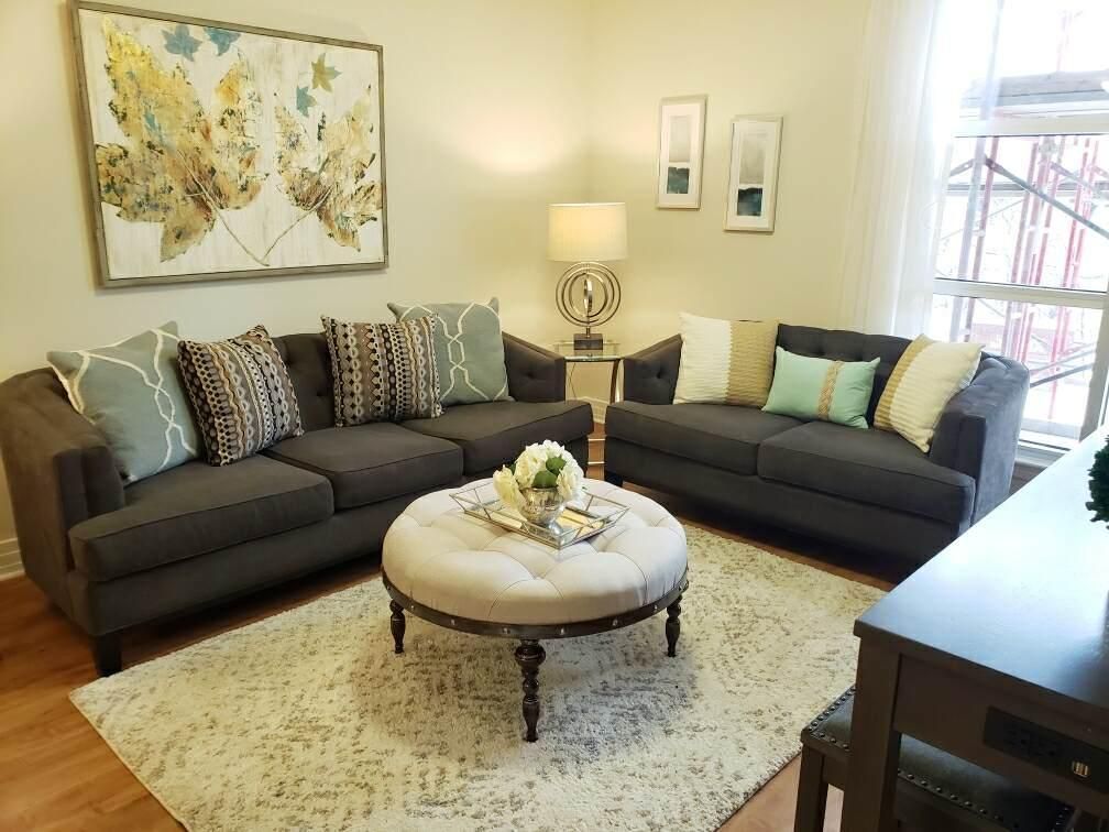 A cozy living room with two gray sofas, a round upholstered coffee table, decorative pillows, and artwork on the walls.