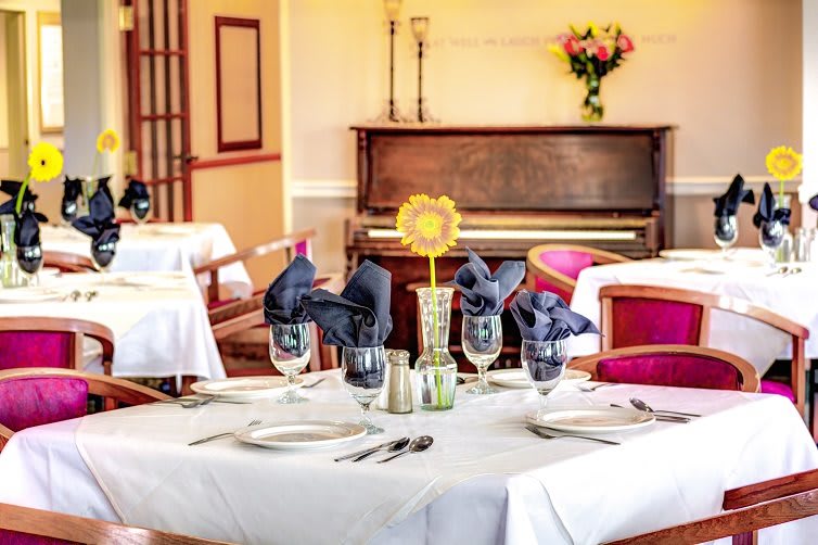 A beautifully set dining table in an elegant restaurant with a piano in the background.