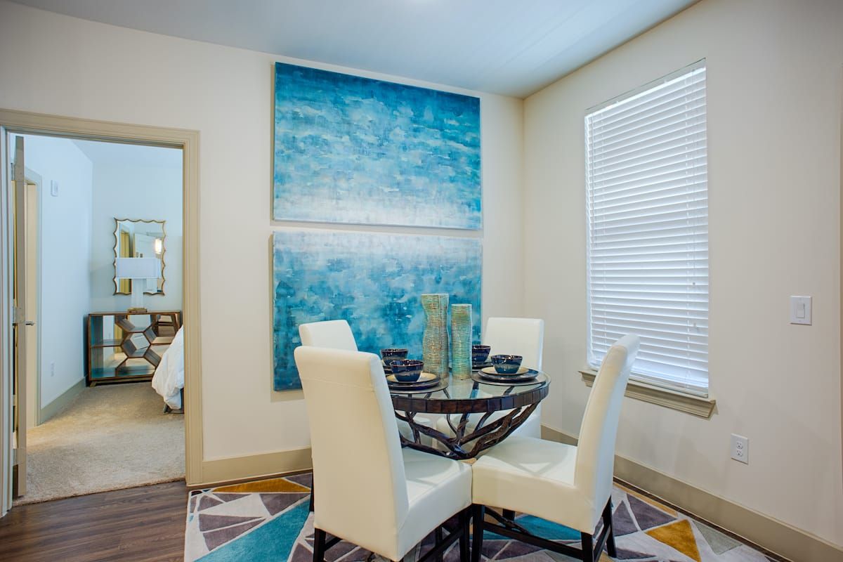 A modern dining room with a round table, white chairs, and a large abstract painting on the wall.