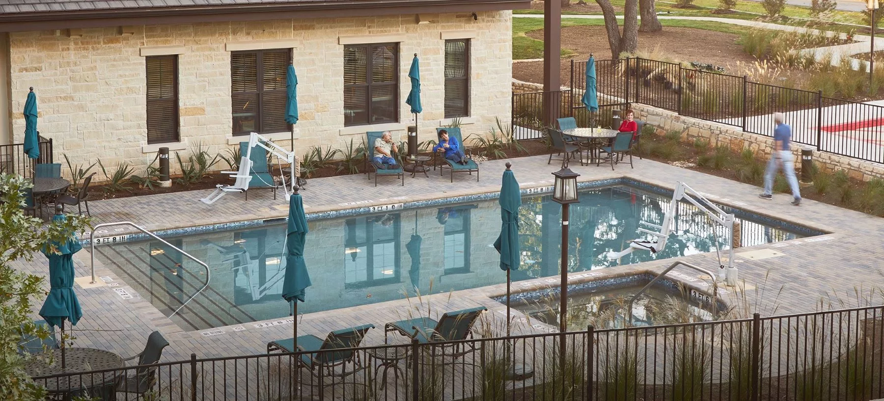 People relaxing by an outdoor swimming pool with deck chairs and umbrellas.
