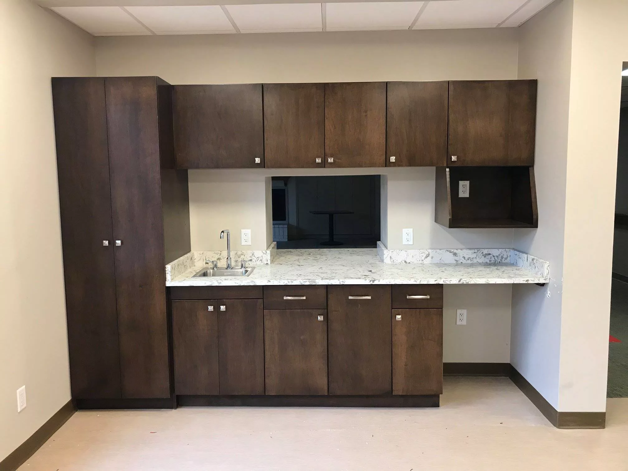 A modern kitchenette with brown cabinets and a countertop sink.