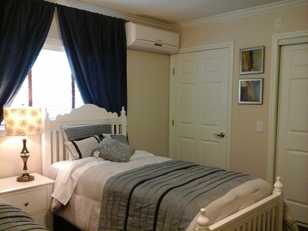 A cozy bedroom with a single bed, dark curtains, and an air conditioner.
