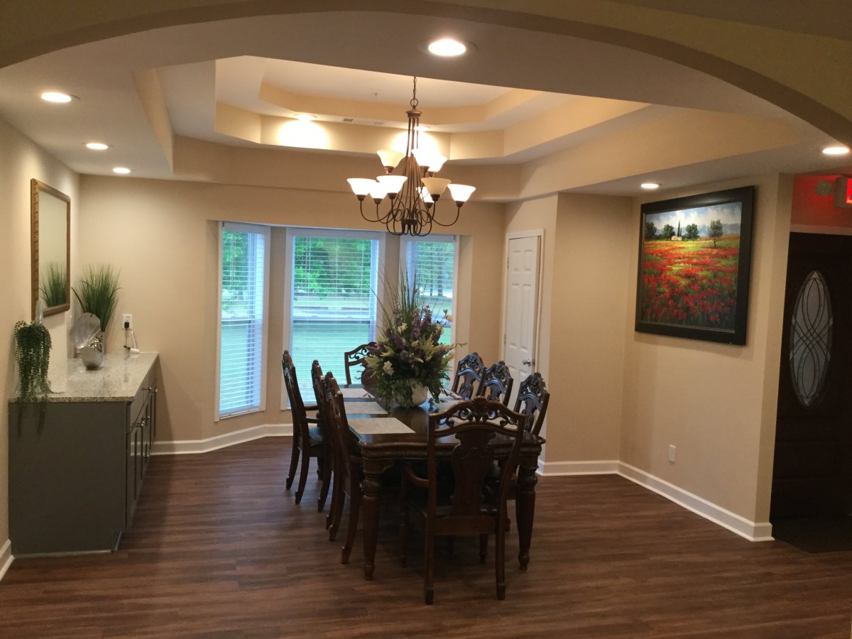 A beautifully designed dining room with a chandelier, wooden flooring, and elegant furniture, complemented by large windows and artwork.