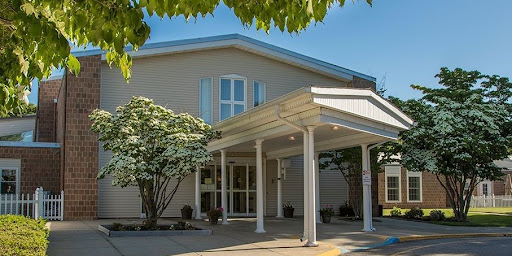 A welcoming entrance of a modern building surrounded by greenery under a clear blue sky.