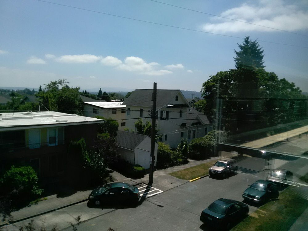 A suburban street with several houses, parked cars, and trees under a clear sky.