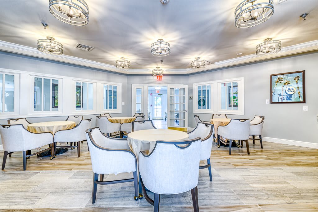 A modern and elegantly designed dining room with white chairs, round tables, and decorative chandeliers.