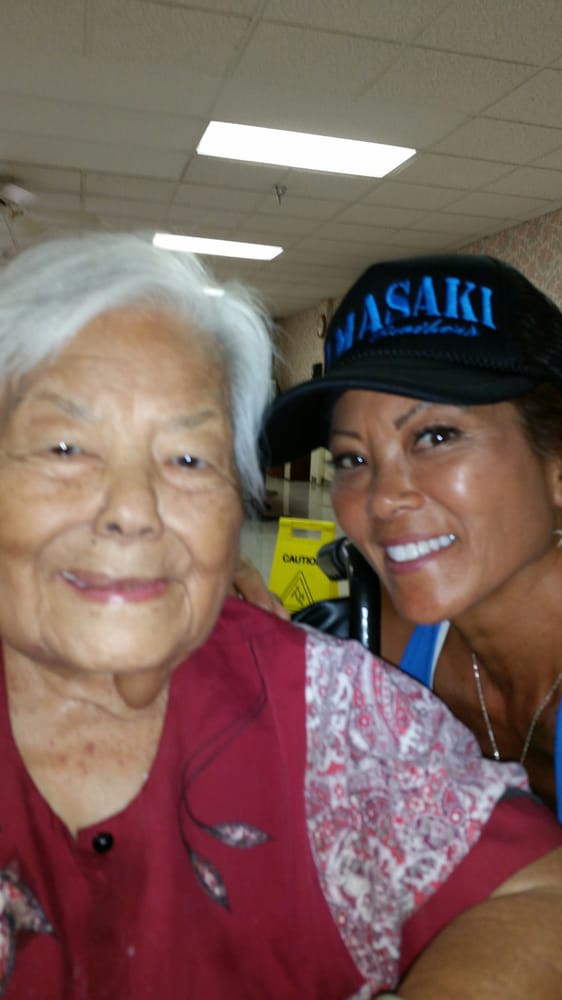 A smiling elderly woman with a younger woman wearing a hat indoors.