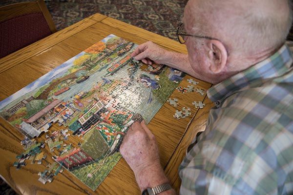 An elderly person working on a colorful jigsaw puzzle at a table.