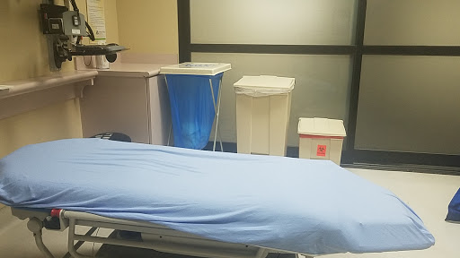 A hospital room featuring a medical bed covered with a blue sheet and waste disposal bins.