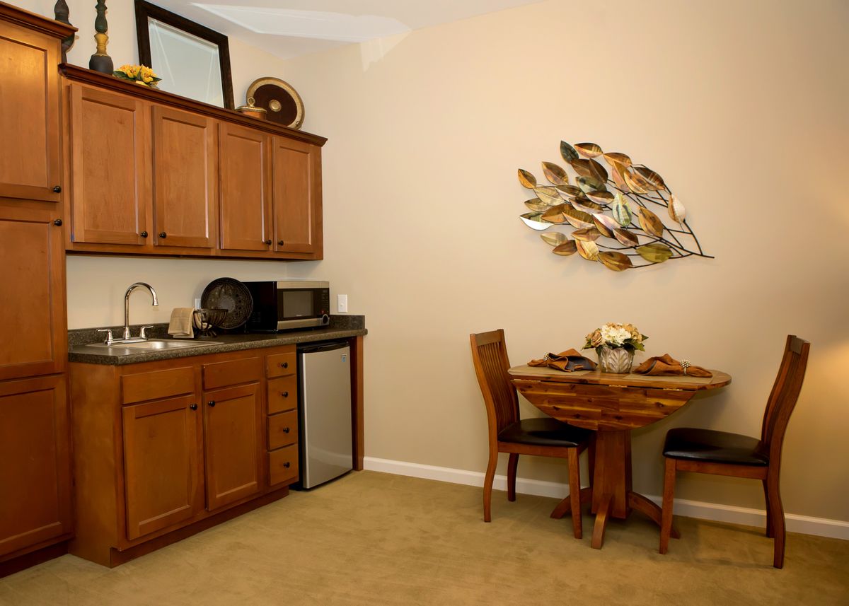 A compact kitchen and dining area with wooden cabinets, a small table and chairs, and decorative wall art.