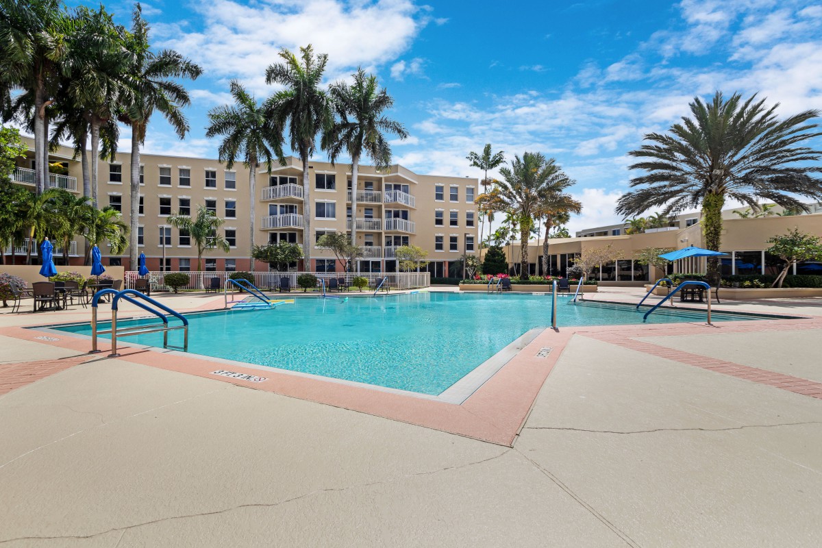 A serene outdoor pool area surrounded by palm trees and a residential building.