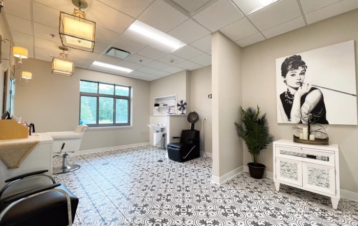 A modern hair salon with stylish decor, featuring a comfortable chair, artwork, and patterned tile flooring.