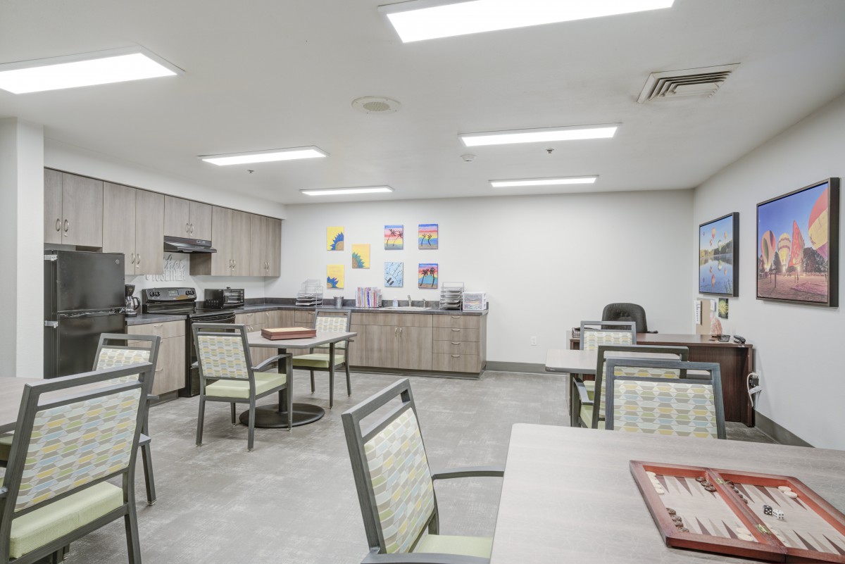 A spacious communal kitchen and dining area with multiple tables and chairs, well-lit by ceiling lights.