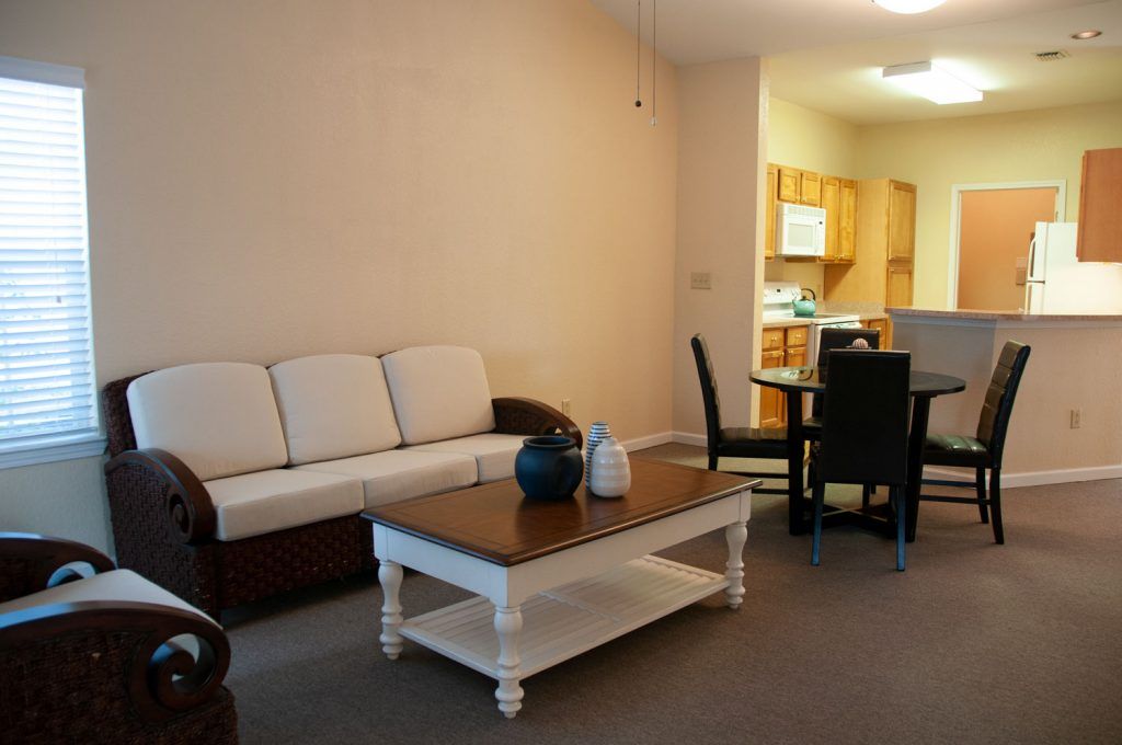 A cozy living room with a sofa, coffee table, and a view into the dining area and kitchen.