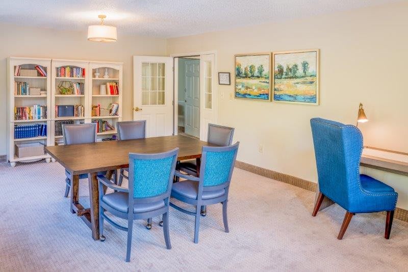 A well-lit conference room with a large table and blue chairs, featuring bookshelves and artwork on the walls.