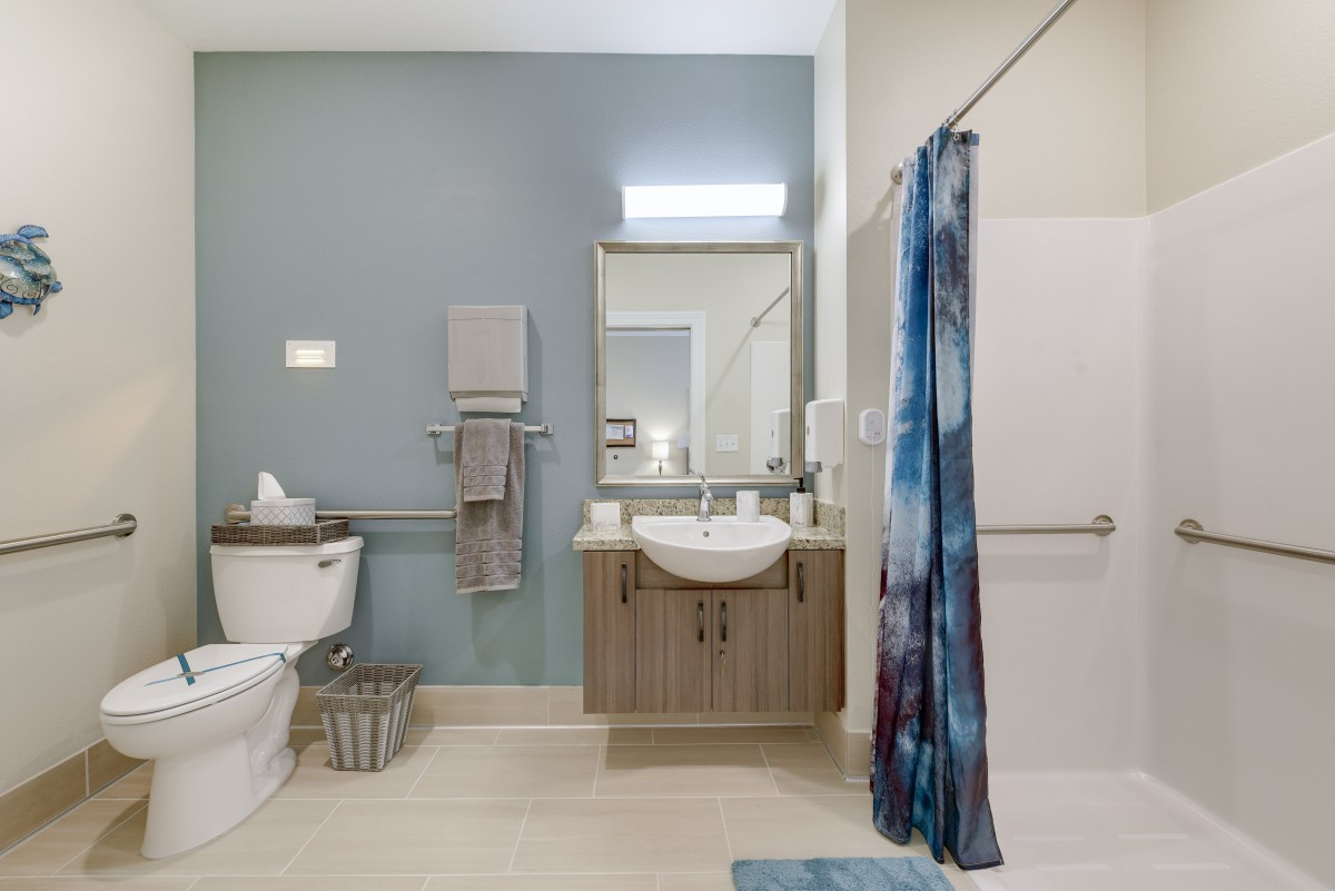 A modern bathroom with a central mirror and sink, featuring a toilet on the left and a shower area with a blue shower curtain.