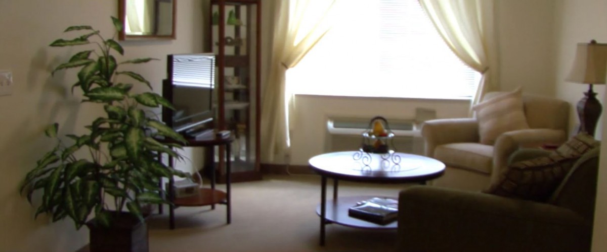 A cozy living room with a TV, coffee table, and sofa near a window with curtains.