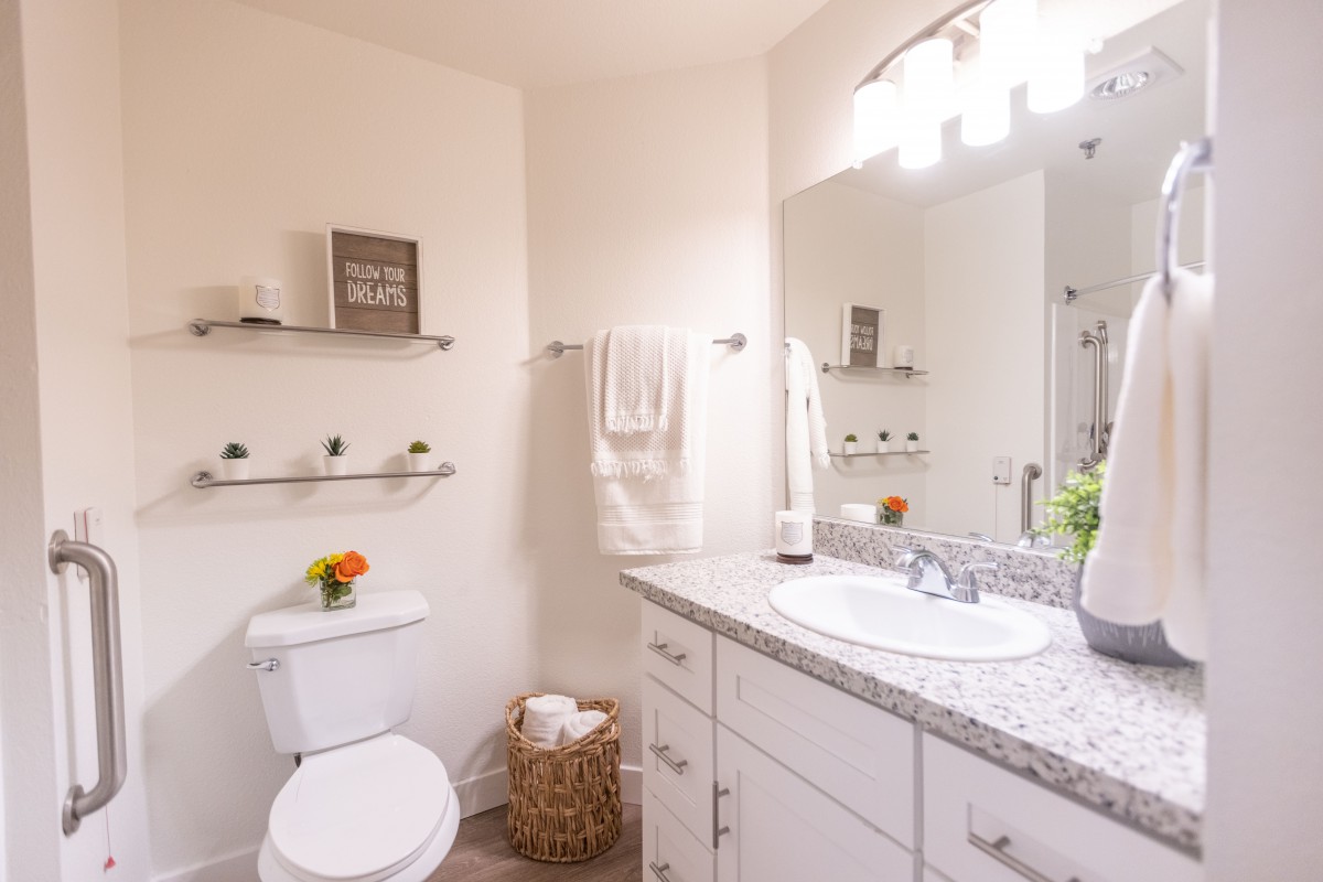 A modern and clean bathroom with bright lighting, featuring a sink, toilet, mirror, and decorative elements.