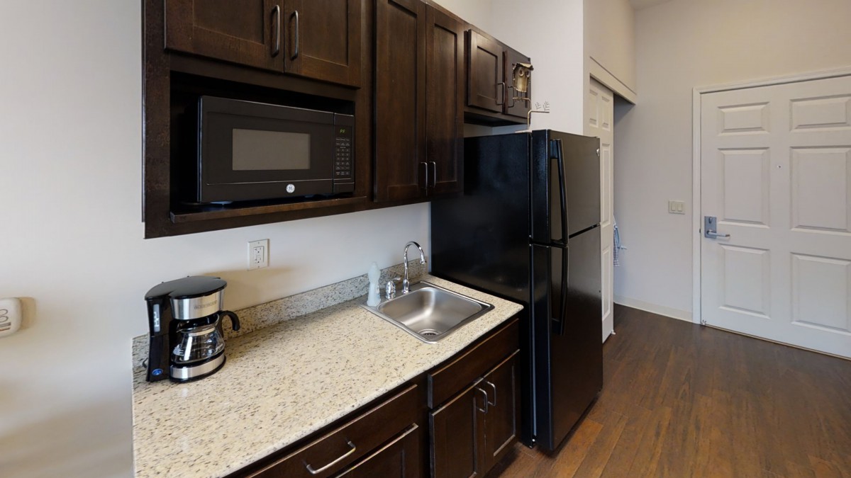 A compact kitchen featuring dark wood cabinets, a microwave, and a coffee maker on the countertop.