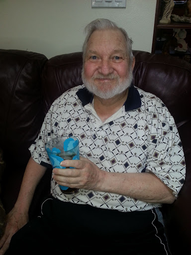 A cheerful man enjoying a colorful drink while seated on a couch.
