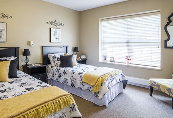 A cozy bedroom with twin beds featuring floral bedding and sunny natural light streaming through the window.