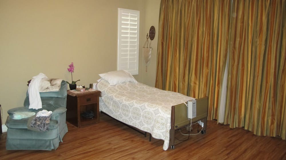 A simple bedroom with a hospital bed, wooden floor, and curtains.
