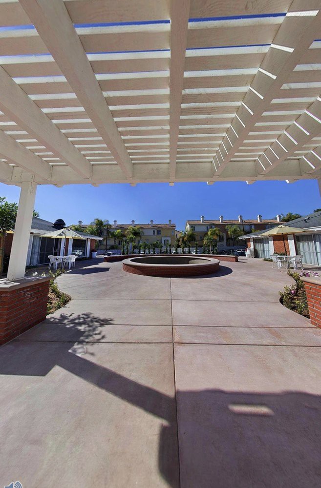 A sunny courtyard featuring a central fountain, surrounded by a pergola and outdoor seating areas.